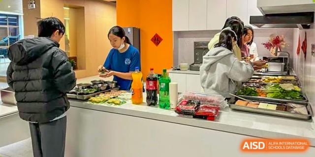 A female staff member in a blue shirt prepares food on a countertop in a bright orange kitchen area at Sias International School.
