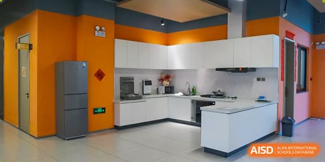 Wide view of a clean, modern kitchen area at Sias International School with white cabinets and bright orange accent walls.