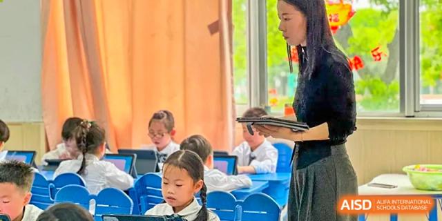 A teacher is interacting with young students in a classroom at SUZHOU INTERNATIONAL FOREIGN LANGUAGE SCHOOL.