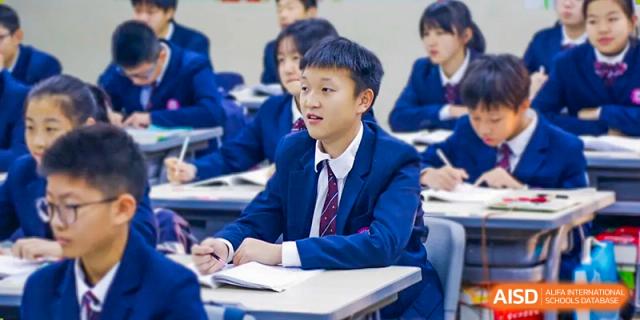 A male student in a dark blue blazer and tie is sitting at a desk and listening to a class at SUZHOU INTERNATIONAL FOREIGN LANGUAGE SCHOOL.