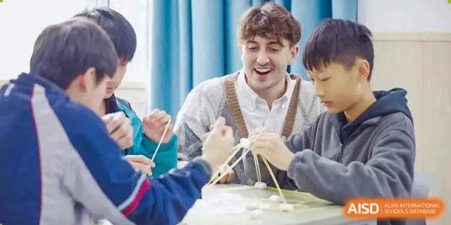 A smiling male teacher is working on a hands-on project with students at SUZHOU INTERNATIONAL FOREIGN LANGUAGE SCHOOL.