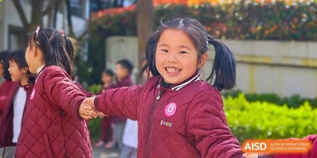 A young girl with pigtails and a red jacket is smiling at the camera at SUZHOU INTERNATIONAL FOREIGN LANGUAGE SCHOOL.
