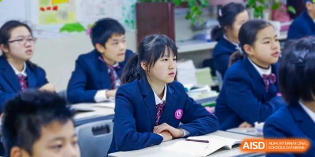 A female student in a dark blue uniform is sitting attentively at her desk in a classroom at SUZHOU INTERNATIONAL FOREIGN LANGUAGE SCHOOL.