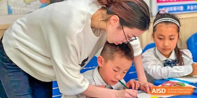 A female teacher is leaning over to help a young male student with his schoolwork at SUZHOU INTERNATIONAL FOREIGN LANGUAGE SCHOOL.