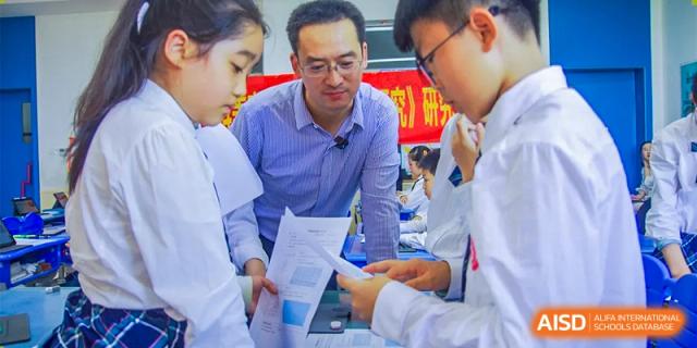 A male teacher is helping two students with their schoolwork, looking at some papers together at SUZHOU INTERNATIONAL FOREIGN LANGUAGE SCHOOL.