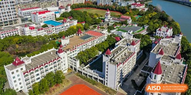 An aerial view of the SUZHOU INTERNATIONAL FOREIGN LANGUAGE SCHOOL campus, showing multiple white buildings with red roofs, green trees, and sports fields.