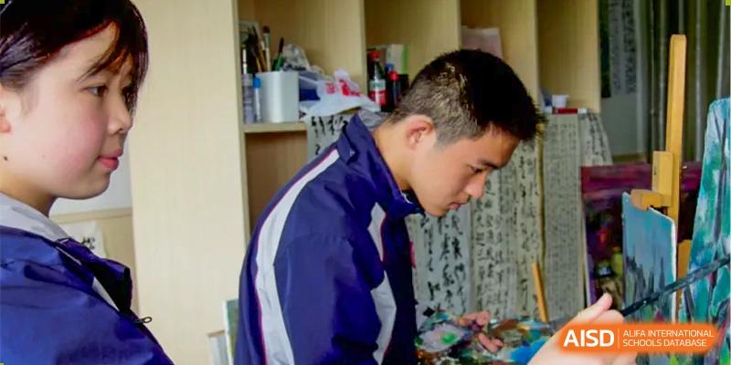 A male student in a dark blue and white jacket is looking down and writing at SUZHOU INTERNATIONAL FOREIGN LANGUAGE SCHOOL.