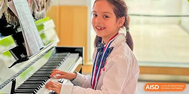 A young girl with a ponytail smiles while sitting at a piano at SUZHOU INTERNATIONAL FOREIGN LANGUAGE SCHOOL.