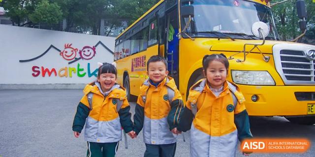 Four smiling young students in yellow jackets standing in front of a yellow school bus at SUZHOU INTERNATIONAL FOREIGN LANGUAGE SCHOOL.