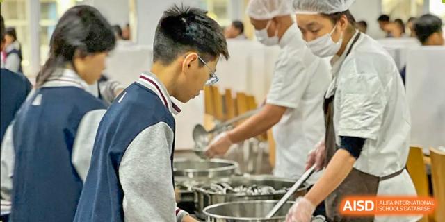 A person is serving food from a large pot in the cafeteria at SUZHOU INTERNATIONAL FOREIGN LANGUAGE SCHOOL.