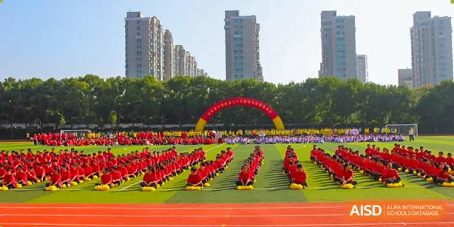 A large group of students from The Experimental School Affiliated to Nanjing Normal University is performing a synchronized routine on a red sports field.