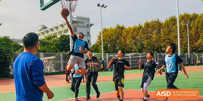 Students from The Experimental School Affiliated to Nanjing Normal University playing basketball with one player jumping for a dunk.