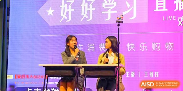 Two female students from The Experimental School Affiliated to Nanjing Normal University are on a stage with a screen behind them that says "好好学".