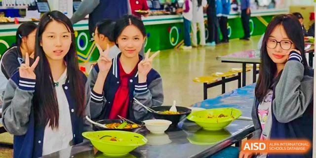 A student at The Experimental School Affiliated to Nanjing Normal University smiling and giving a peace sign in a cafeteria.