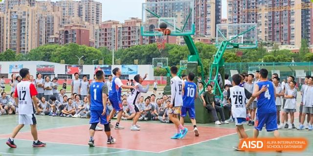 Weiming School Chengdu Qingbaijiang students play a lively game of basketball on an outdoor court, with spectators watching from the sidelines.