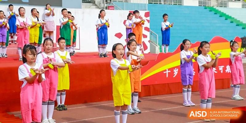 Weiming School Chengdu Qingbaijiang elementary students perform a song on a stage during a school event.