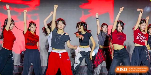 Weiming School Chengdu Qingbaijiang students perform a choreographed dance on a stage with a red background.