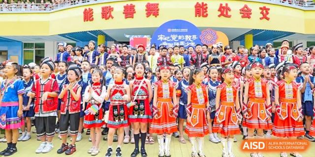 Weiming School Chengdu Qingbaijiang students wearing traditional ethnic clothing pose for a group photo outdoors in front of a school banner.
