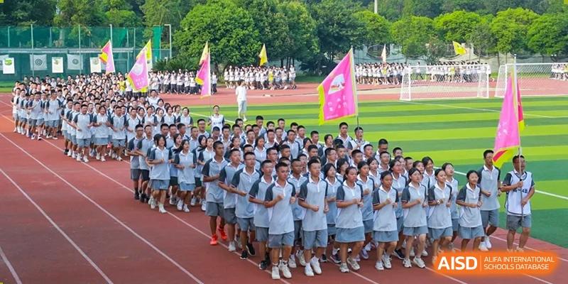 A large group of Weiming School Chengdu Qingbaijiang students in uniform stands in formation on a track field, with a crowd of students in the background.
