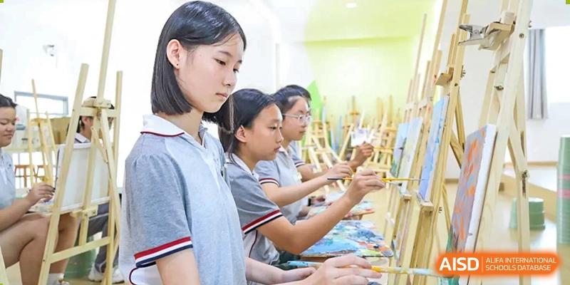 Weiming School Chengdu Qingbaijiang students sit at easels in an art classroom, painting on canvases.