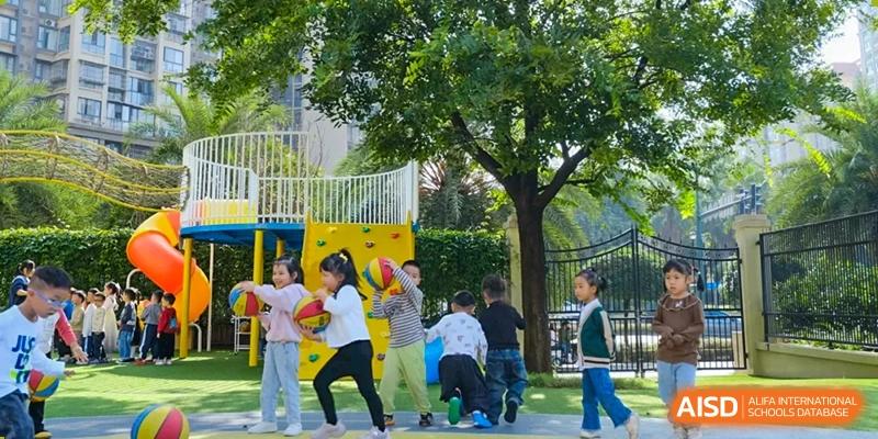 Weiming School Chengdu Qingbaijiang students play with balls and hula hoops on a colorful outdoor playground surrounded by trees.