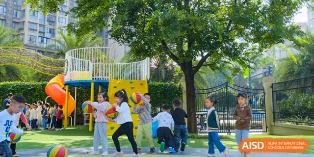 Weiming School Chengdu Qingbaijiang students play with balls and hula hoops on a colorful outdoor playground surrounded by trees.
