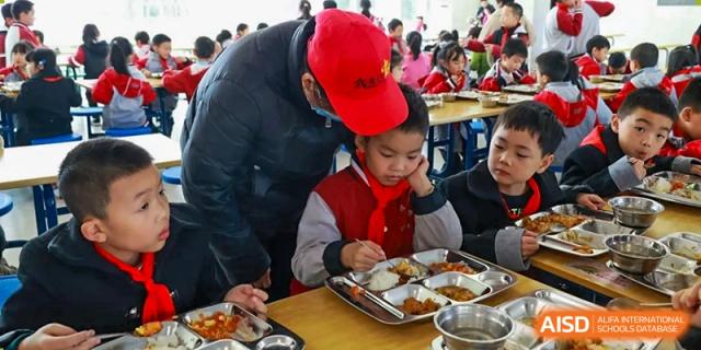 A student from Weiming School Chengdu Qingbaijiang eating lunch while a staff member helps them.