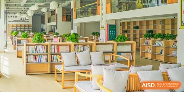 A bright, comfortable reading nook or common area with white chairs, cushions, and many plants on shelving at Weiming School Shenzhen Nanshan.