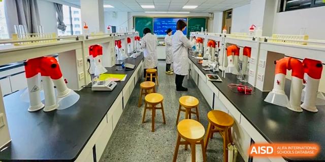 Students in white lab coats working in a brightly lit science laboratory with tall benches and stools at Weiming School Shenzhen Nanshan.