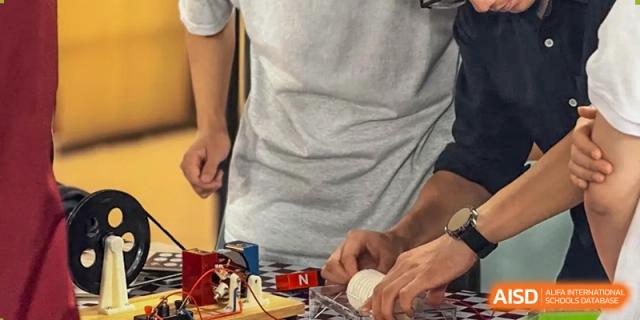 A close-up shot of hands working on a small robotics or electronics project in a classroom at Weiming School Shenzhen Nanshan.