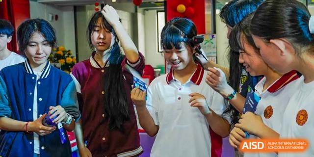 Two happy students holding up small electronic components or projects in a classroom at Weiming School Shenzhen Nanshan.
