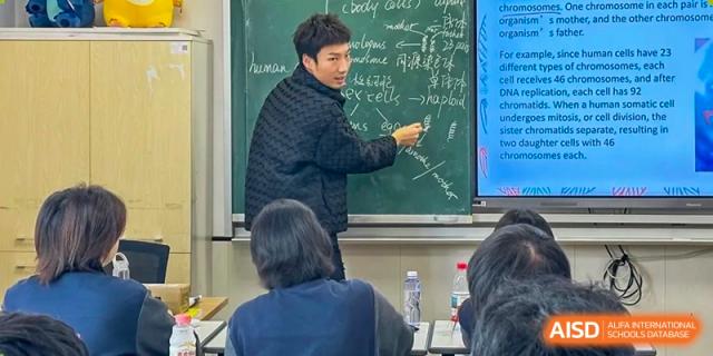 A male teacher writing or pointing at a difficult equation on a chalkboard while students look on in a math or science class at Weiming School Shenzhen Nanshan.