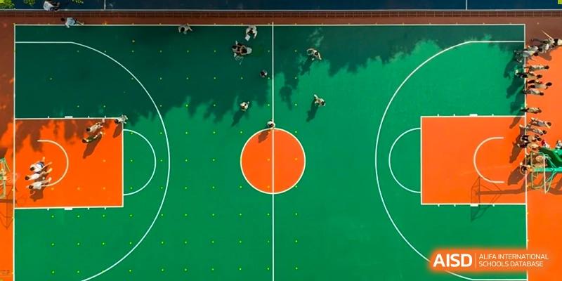 An overhead, aerial view of students playing basketball on a bright green court with an orange center circle at Weiming School Shenzhen Nanshan.