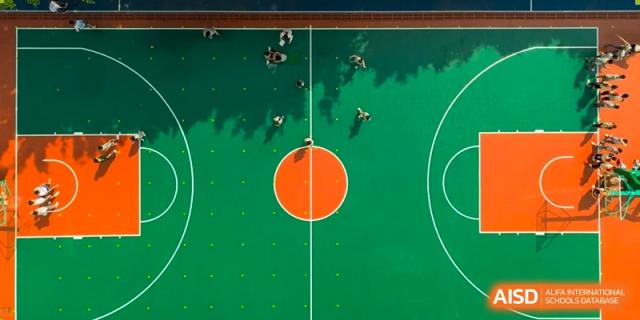 An overhead, aerial view of students playing basketball on a bright green court with an orange center circle at Weiming School Shenzhen Nanshan.