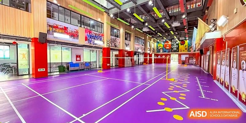 The interior of a large, modern indoor gymnasium with a bright purple floor set up for badminton or volleyball at Weiming School Shenzhen Nanshan.
