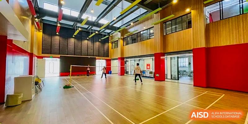 Students playing badminton on an indoor wooden court with high ceilings at Weiming School Shenzhen Nanshan.