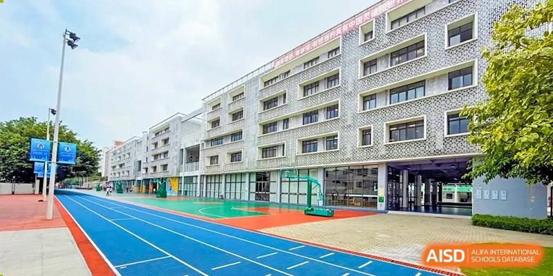 The exterior of a modern school building with a nearby blue running track and an outdoor basketball court at Weiming School Shenzhen Nanshan.