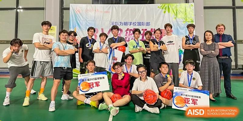 A group of happy students and adults posing on the ground with a basketball and a championship banner at Weiming School Shenzhen Nanshan.