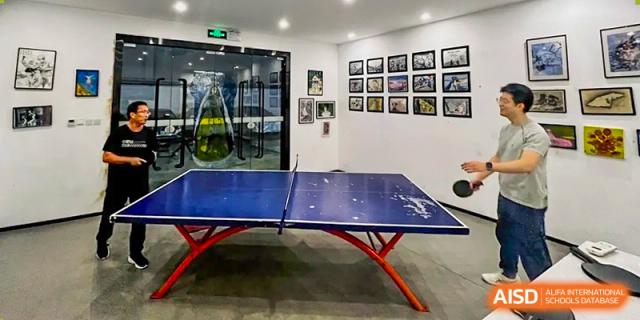 An indoor table tennis (ping pong) room with a blue table and framed pictures on the wall at Weiming School Shenzhen Nanshan.
