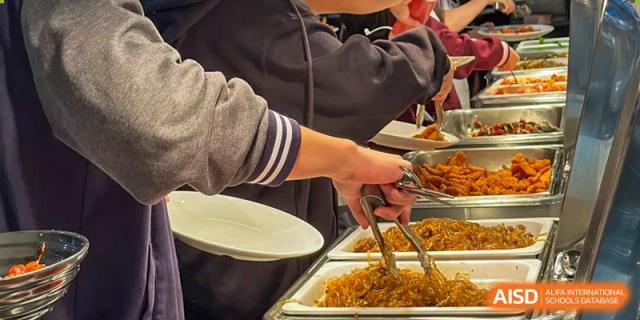 A student serving themselves food from a buffet line onto a plate in the school cafeteria at Weiming School Shenzhen Nanshan.