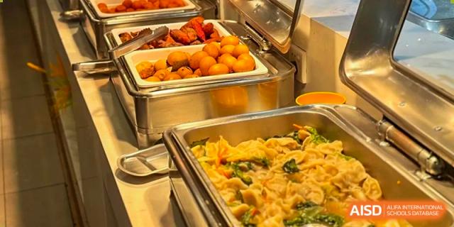 A close-up of a serving tray filled with various hot food items, including stir-fries and chicken, in the cafeteria at Weiming School Shenzhen Nanshan.