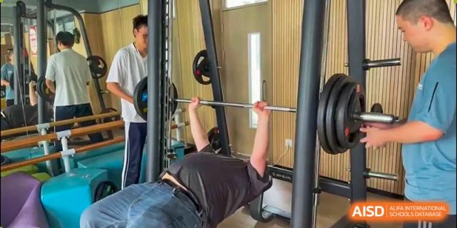 A student performing a bench press in the school's weight training or fitness center at Weiming School Shenzhen Nanshan.