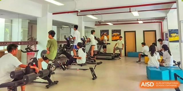 Students using treadmills and elliptical machines in a well-equipped indoor gym or fitness center at Weiming School Shenzhen Nanshan.