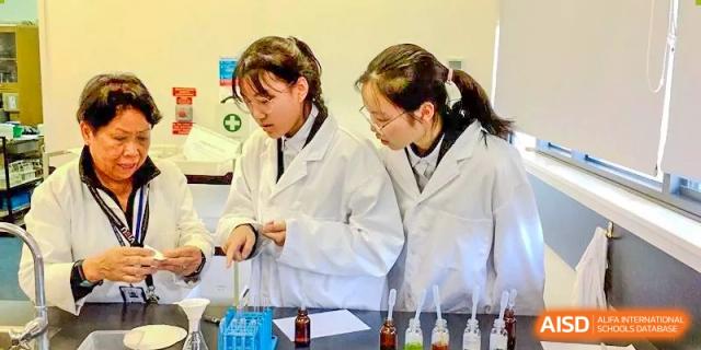Students in lab coats working with beakers and chemicals in the science lab at Wenzhou No.21 Middle School.
