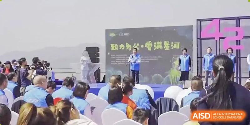 An adult speaker addresses children seated on the floor, with Chinese text on a screen behind, likely a school assembly at Wenzhou No.21 Middle School.
