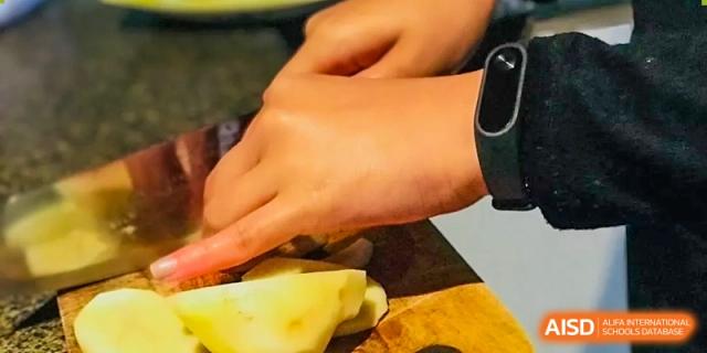Close-up of hands chopping a yellow vegetable on a cutting board, part of a cooking class at Wenzhou No.21 Middle School.