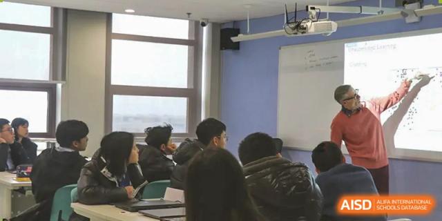 A small group of students facing away from the camera, listening to a lecture or presentation in a classroom at Wuhan Optics Valley ULINK School.