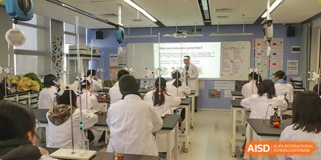 Students wearing lab coats watching a teacher give a presentation in a bright science laboratory at Wuhan Optics Valley ULINK School.