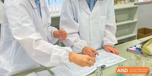 A close-up of students' hands in lab coats working together to review documentation or data in a science class at Wuhan Optics Valley ULINK School.