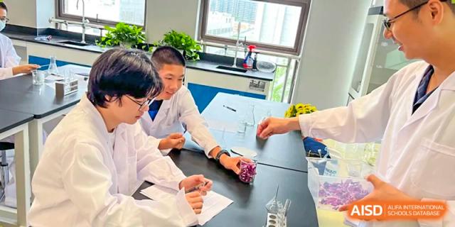 A small group of students collaborating on a hands-on project at a bright outdoor table, reviewing small components, at Wuhan Optics Valley ULINK School.